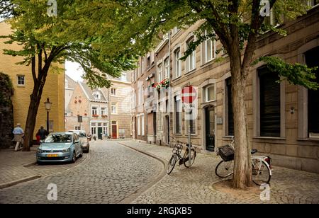 street in old districts of Maastricht on Sunday afternoon. Narrow street in old dutch town with few pedestrians and parked cars and bicycles. Stock Photo