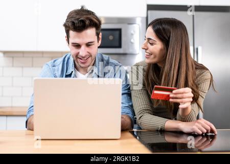 young couple planning vacations together at home looking a laptop. two cheerful young adults sitting on the kitchen. finance concept Stock Photo