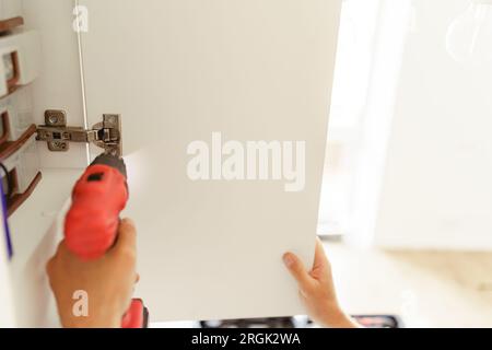 Close up of professional repairman is using a screwdriver to adjust door of cabinet in kitchen Stock Photo