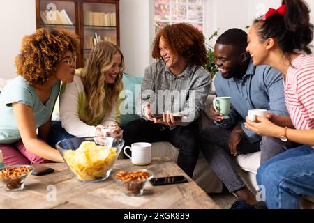 Happy diverse group of friends using smartphone with snacks on table at home Stock Photo