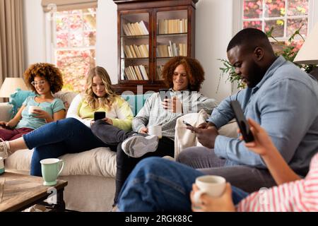 Happy diverse group of friends using smartphones with cups of coffee at home Stock Photo