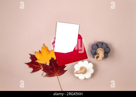 Pink envelope with empty white card for text, autumn leaves and decorative pumpkins on beige background. Blank invitation or greeting card mockup with Stock Photo