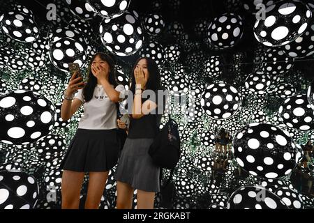 Hong Kong, China. 10th Aug, 2023. Two girls take selfies inside the art installation ”Dots Obsession: Aspiring to Heaven's Love' at M  Visual Culture Museum in Hong Kong. The artwork by Japanese artist Yayoi Kusama, who has lived in the United States between 1958 and 1975, features her famous polka dots and reflective mirrors inside a cubic environment which offers a kaleidoscopic visual experience. (Credit Image: © Daniel Ceng Shou-Yi/ZUMA Press Wire) EDITORIAL USAGE ONLY! Not for Commercial USAGE! Stock Photo