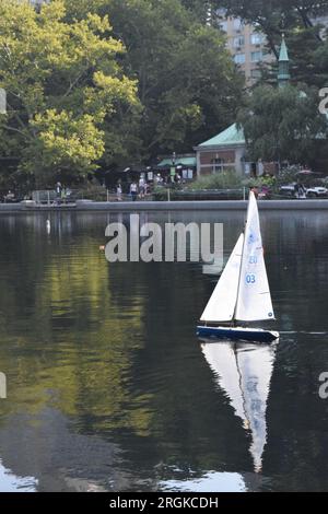 A toy boat sailing on Conservatory Water, the boat pond in Central Park, New York, with the Boathouse in the background. Stock Photo