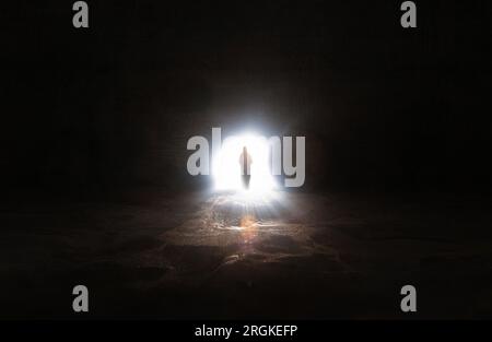 The resurrected Jesus walks out of the tomb with the stone door opened and bright light shining through and the cross of Jesus Christ Love and death a Stock Photo