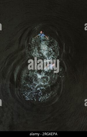Top view of anonymous cheerful male students in school uniform swimming in rough wavy water of dark pond by evening Stock Photo
