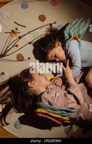 High angle of cute little girls with wing costume lying over cotton mat on floor in illuminated room while sleeping Stock Photo