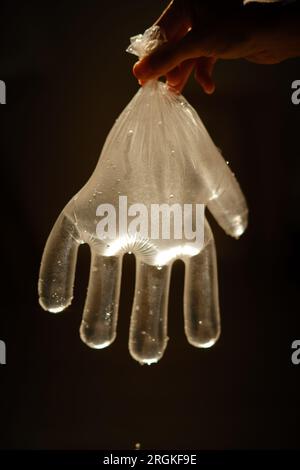 Crop unrecognizable person showing plastic glove with water and drops in shiny light on black background Stock Photo