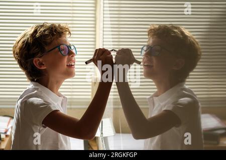 Side view of cheerful schoolboy taking notes on whiteboard during lesson in classroom at school Stock Photo