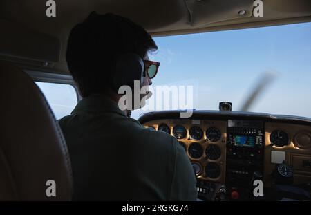 Back view focused male aviator in headphones and sunglasses flying modern helicopter in cloudless blue skies Stock Photo