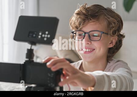 Smiling preteen child in glasses shooting video for online blog using professional equipment in modern living room at home Stock Photo