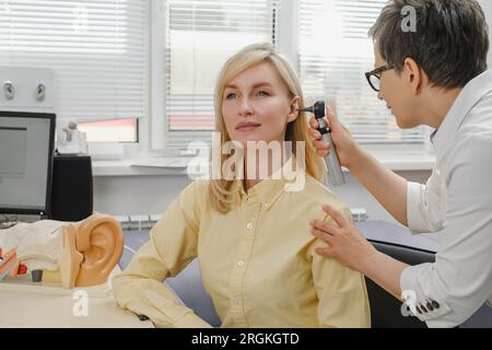 Woman patient having check-up of hearing at doctor otolaryngologist. Hearing exam for female. Otolaryngologist doctor checking mature woman's ear Stock Photo