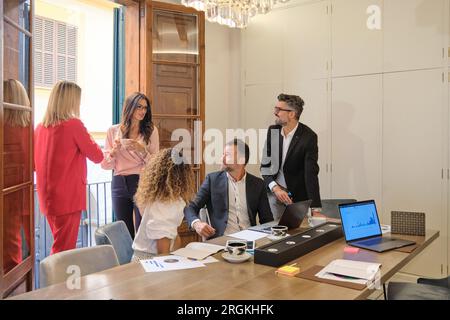 Group of cheerful female and male colleagues in formal clothes talking during break in office Stock Photo