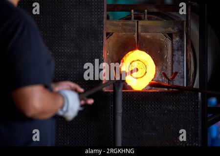 Crop anonymous male worker putting iron rod with attached glass object in furnace at factory during production process Stock Photo