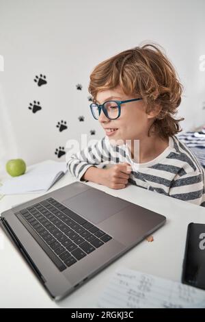 Smart curly haired child using netbook and looking at screen while browsing social media in bedroom at home Stock Photo