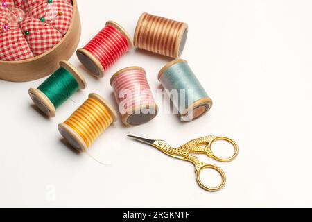 A gold plated stork scissors and colored threads spools on a white background with copy space Stock Photo