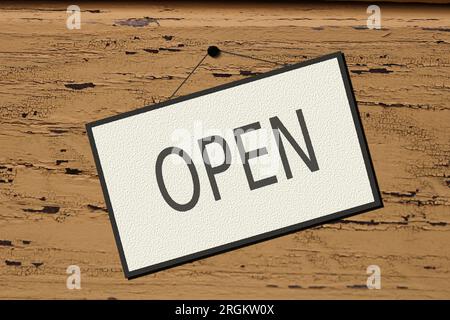 White panel with the word OPEN written in black letters. Weathered painted wooden background with peeling paint, brown background, white sign. Stock Photo