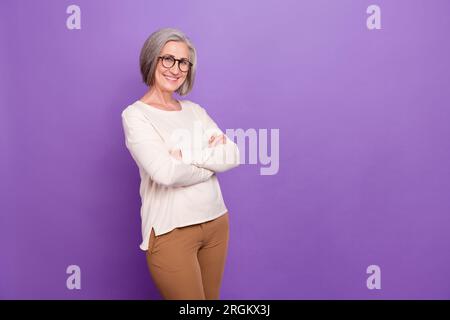 Portrait of charming middle age lady hold crossed arms toothy smiling near mockup empty space isolated purple color background Stock Photo