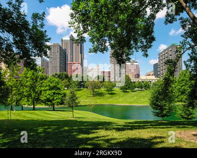 A park with trees and a lake in front of the St. Louis skyline. The park is lush and green, and the lake is calm and reflective. Stock Photo