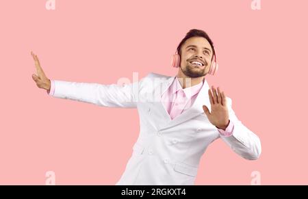 Cheerful handsome young man in white suit and headphones listening to music and dancing Stock Photo