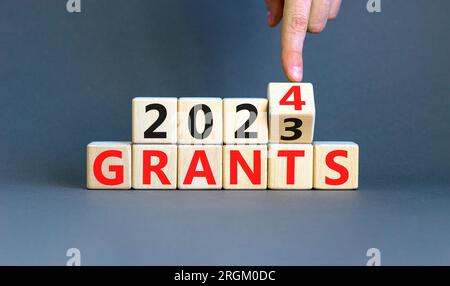 Planning 2024 grants new year symbol. Businessman turns a wooden cube and changes words Grants 2023 to Grants 2024. Beautiful grey background, copy sp Stock Photo