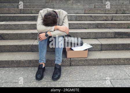 The unhappy manager was fired from his job. A sad worker sits on the steps of a business center after being laid off, crisis, depression. Stock Photo