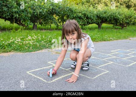 Little girl draws with chalk on the pavement in the park Stock Photo