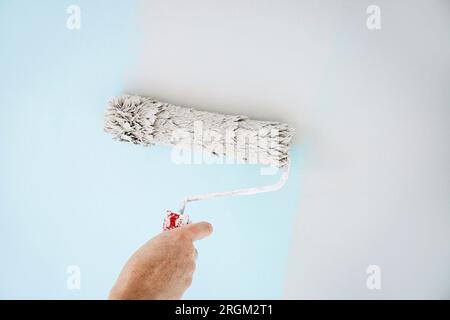 Man worker using paint roll to repaint old wall paint, rolling tool. Blue to neutral gray. Home indoors. Stock Photo
