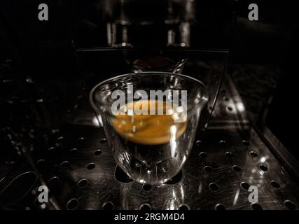 Glass cup with freshly brewed black coffee with foam and golden cream with bubbles visible through the transparency of the cup of a fully automatic es Stock Photo