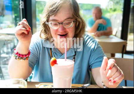 Portrait of a 40 yo woman with the Down Syndrome drinking a strawberry milkshake, Meerhout, Belgium Stock Photo