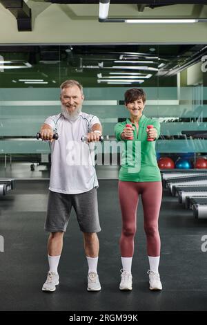 positive elderly couple, happy man and woman training with dumbbells, husband and wife in gym Stock Photo