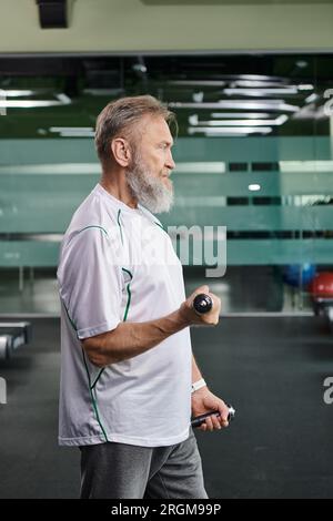 side view of bearded elderly man exercising with dumbbells in gym, active senior, fitness routine Stock Photo