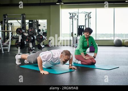 elderly man with beard doing plank, happy woman exercising in gym, fitness mats, active seniors Stock Photo