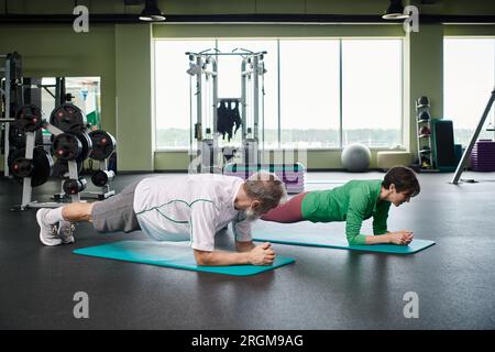 elderly man and woman doing plank on fitness mats, active seniors exercising on in gym, healthy life Stock Photo