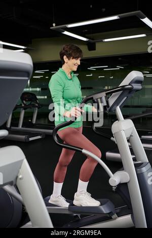 active senior, happy elderly woman in sportswear exercising in gym, using stepper exercise machine Stock Photo