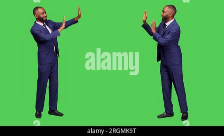 African american employee pushing something aside, showing rejection for an object to left or right sides of studio. Male startup entrepreneur refusing thing over green screen backdrop. Stock Photo