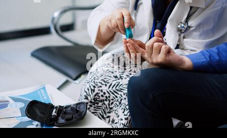 Elderly medic taking insulin level test using glucometer in hospital reception, doing diabetes examination to measure glucose from patient blood sample. Senior man having checkup visit appointment Stock Photo