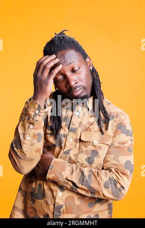 Puzzled man brainstorming job ideas, thinking at solution to solve difficult business problem. Thoughtful african american adult having unsure expression, standing in studio over yellow background Stock Photo
