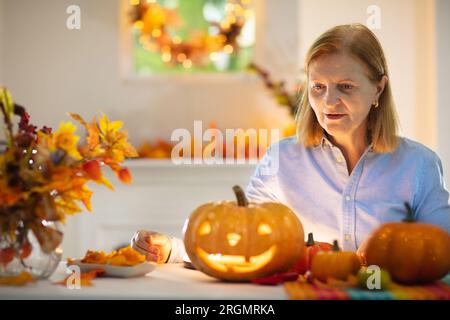 Family carving pumpkin for Halloween celebration. Senior woman cutting jack o lantern for traditional trick or treat decoration. Stock Photo
