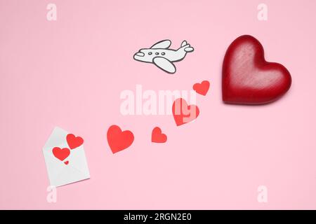 Long-distance relationship concept. Decorative hearts flying out of envelope and paper airplane on pink background, flat lay Stock Photo