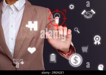 Woman touching light bulb icon in target on digital screen against dark background, closeup Stock Photo