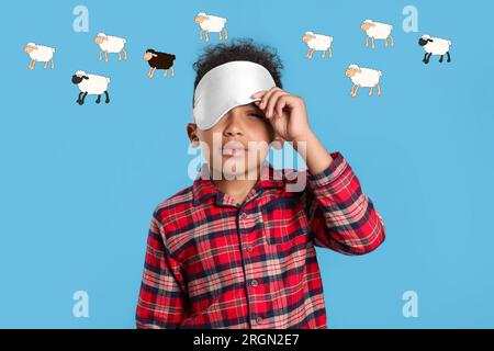 Sleepy boy with blindfold suffering from insomnia on light blue background. Illustrations of sheep above him Stock Photo