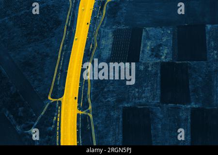Aerial view of dark fields and yellow road . Plowed lands seen from above Stock Photo