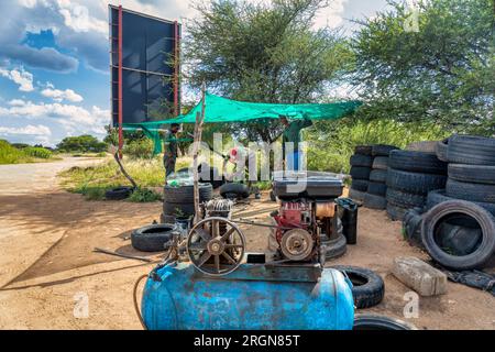 african men, street hustlers behind a compressor, fixing and inflating tires for a living, team of working entrepreneurs in workwear on the side of th Stock Photo