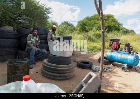 african american street hustlers behind a compressor, fixing and inflating tires for a living, team of workers in workwear Stock Photo