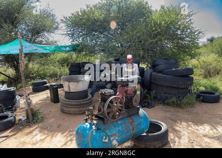 african american street hustlers behind a compressor, fixing and inflating tires for a living, team of workers in workwear Stock Photo