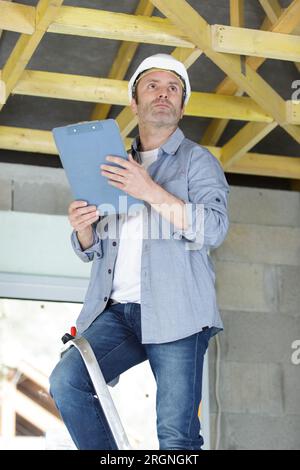 builder standing on ladder while holding a clipboard Stock Photo