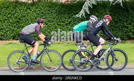 Whittlebury,Northants.,UK - Aug 6th 2023.  Group of three cyclists cycling through an English village on a Sunday morning. Stock Photo