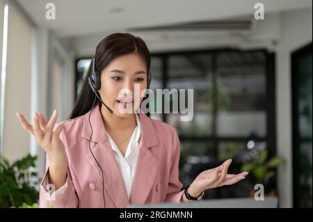 A professional and beautiful Asian female customer service or call-centre agent in headset is having a serious conversation with a customer over the p Stock Photo
