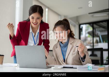 Two cheerful and excited Asian businesswomen are celebrating their project success together in the office. teamwork concept Stock Photo
